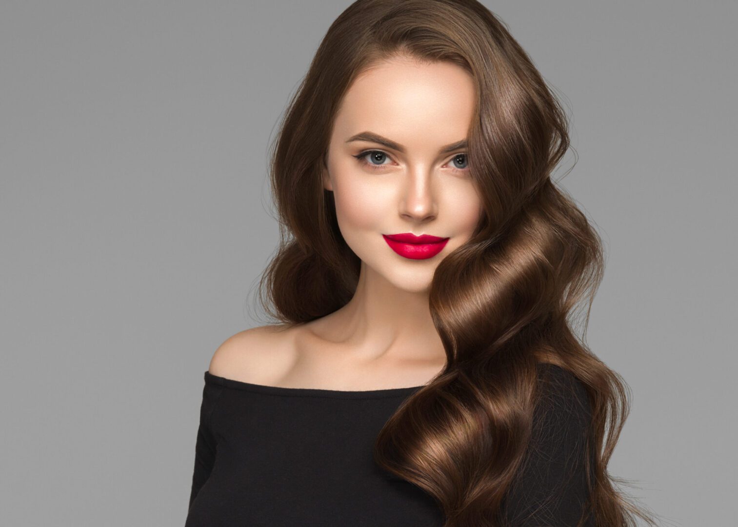 A person with long wavy brown hair and a charming face wearing red lipstick