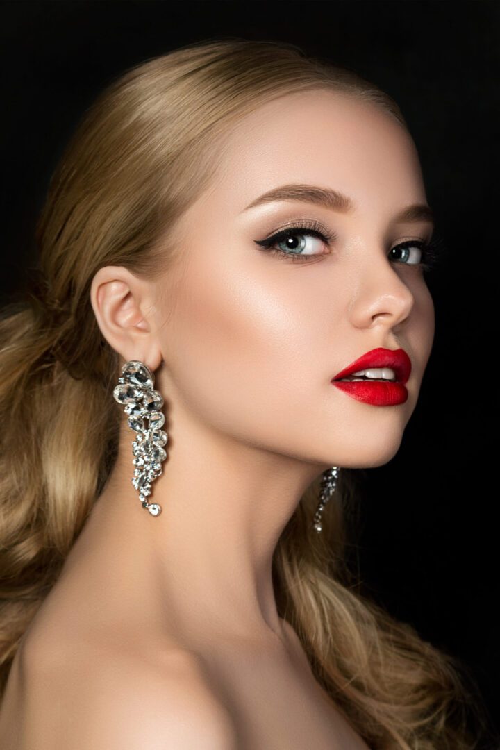 A person wearing stylish makeup with red lips and silver dangling earrings